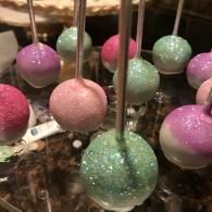 Glittery pink, green, and purple cake pops on sticks in a tray