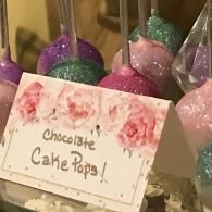 Chocolate cake pops with pink and green glitter and a floral “Chocolate Cake Pops!” sign