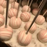 Pink-striped cake pops with chocolate drizzle on sticks in a box