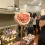 Handheld dessert on a stick with pink topping in a bakery display case