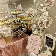 Pastel dessert table with rose decor, tiered sweets, and decorative signs on a pink sequined cloth.