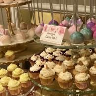 Cupcakes and cake pops displayed on a dessert table with pink, purple, and teal decorations