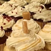 Assorted cupcakes topped with swirled white frosting and caramel candies on display