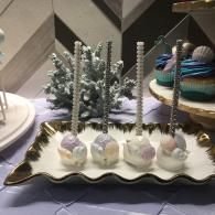 Dessert display with white cake pops, silver sprinkles, and a frosted tree centerpiece on a table