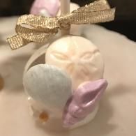 Small white decorated figurine with a gold bow, silver heart, and pink leaf accents