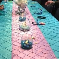 Colorful craft table with glass jars and supplies on pink and teal tablecloths