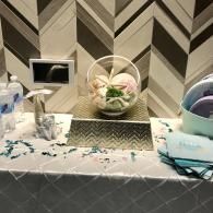 Decorated table with a glass bowl of flowers, small sign, and pastel party favors against chevron wallpaper