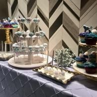 Dessert display on a table with cupcake stands, sweets, and a chevron-pattern backdrop
