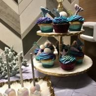 Two-tier dessert stand with blue-frosted cupcakes and a small pinecone centerpiece