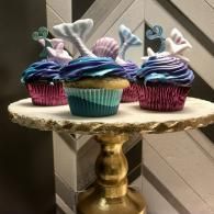 Three colorful cupcakes with pastel frosting and bunny decorations on a gold pedestal stand.