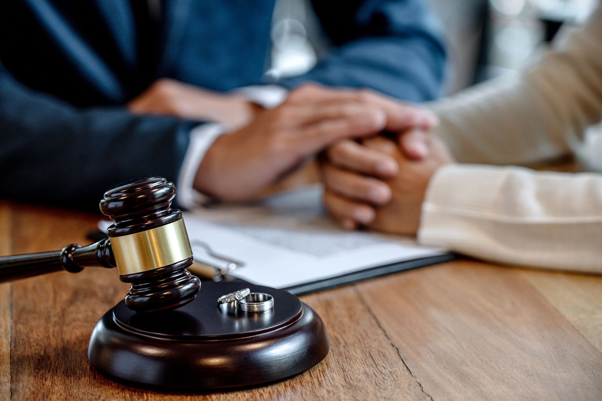 A judge 's gavel with wedding rings on it is sitting on a wooden table next to a couple holding hands.