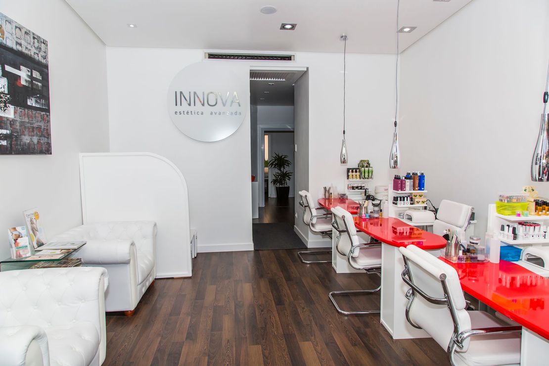 Interior luminoso del salón con estaciones de manicura rojas, sillas blancas y suelo de madera oscura.