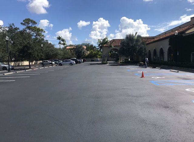 Empty parking lot beside a building under a blue sky, with a few orange cones and parked cars in the distance.