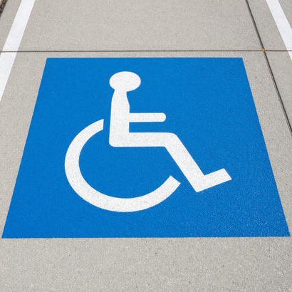 Blue wheelchair accessibility symbol painted on a sidewalk tile.