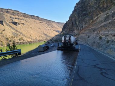 Water tanker truck on a wet canyon road beside a river and steep rocky cliffs.
