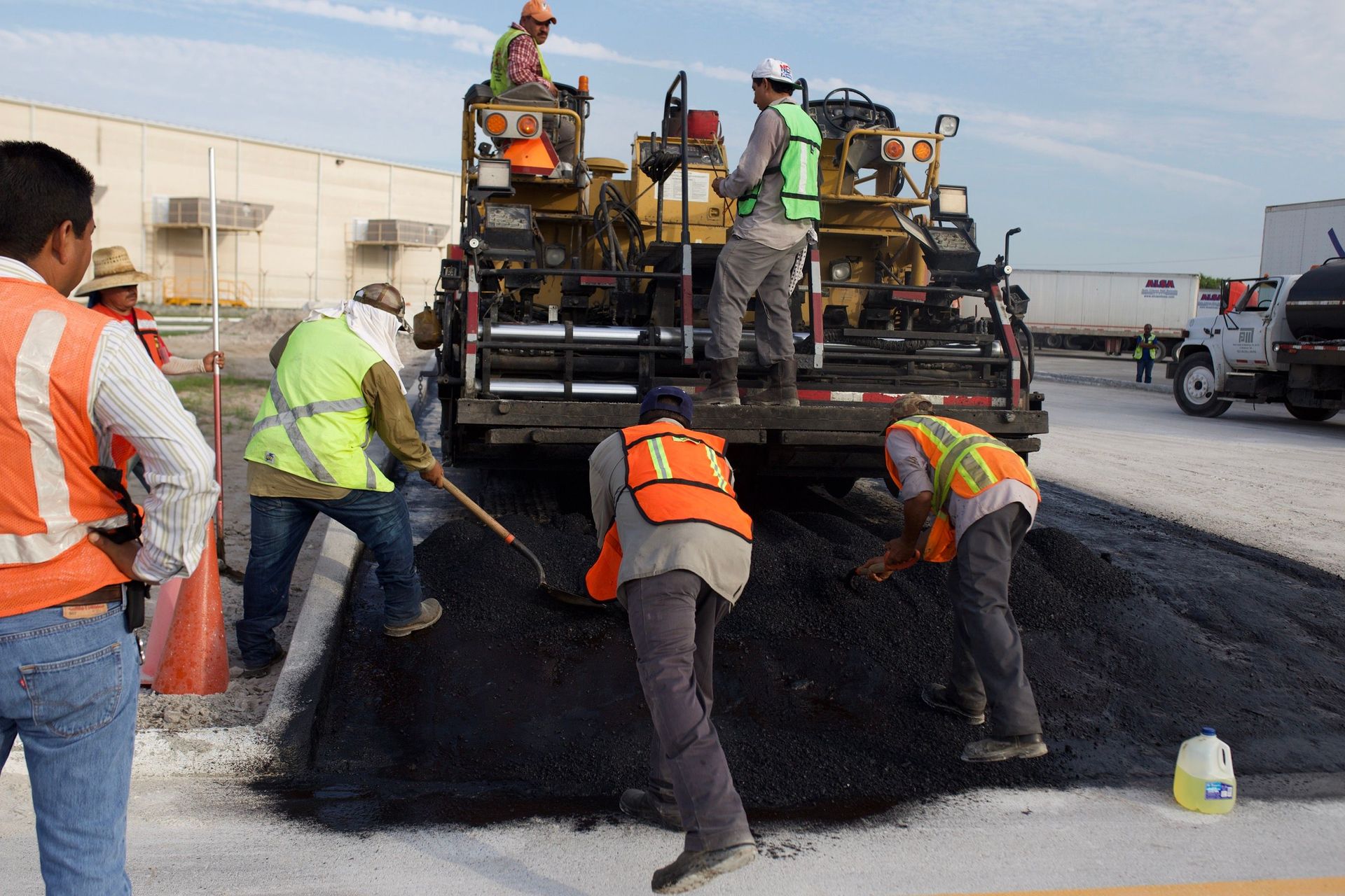 Road crew paving asphalt with a machine and workers in safety vests and helmets