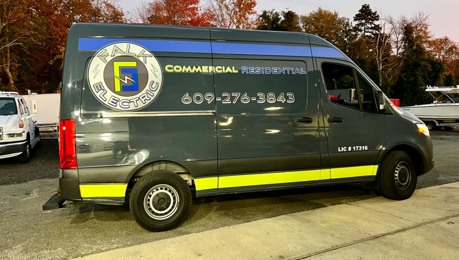 Dark green commercial van with company logo and phone number parked outdoors at dusk.
