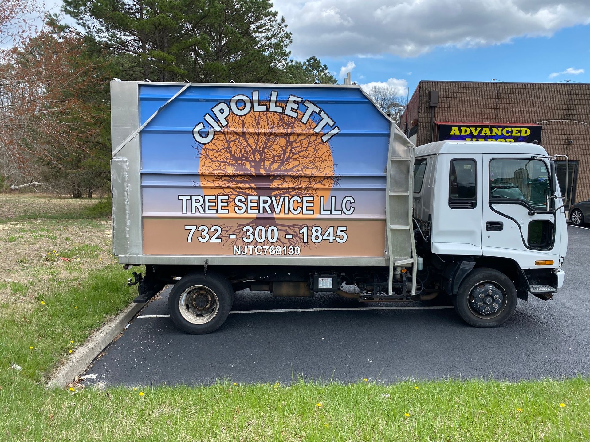 Chipolleta Tree Service LLC truck parked on roadside, blue and tan wrapped box truck with ladder racks