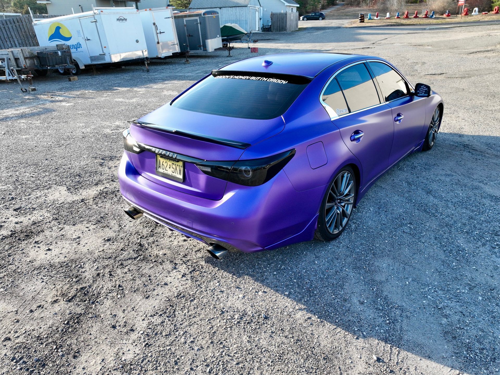 Purple sedan parked on gravel lot with industrial buildings in the background