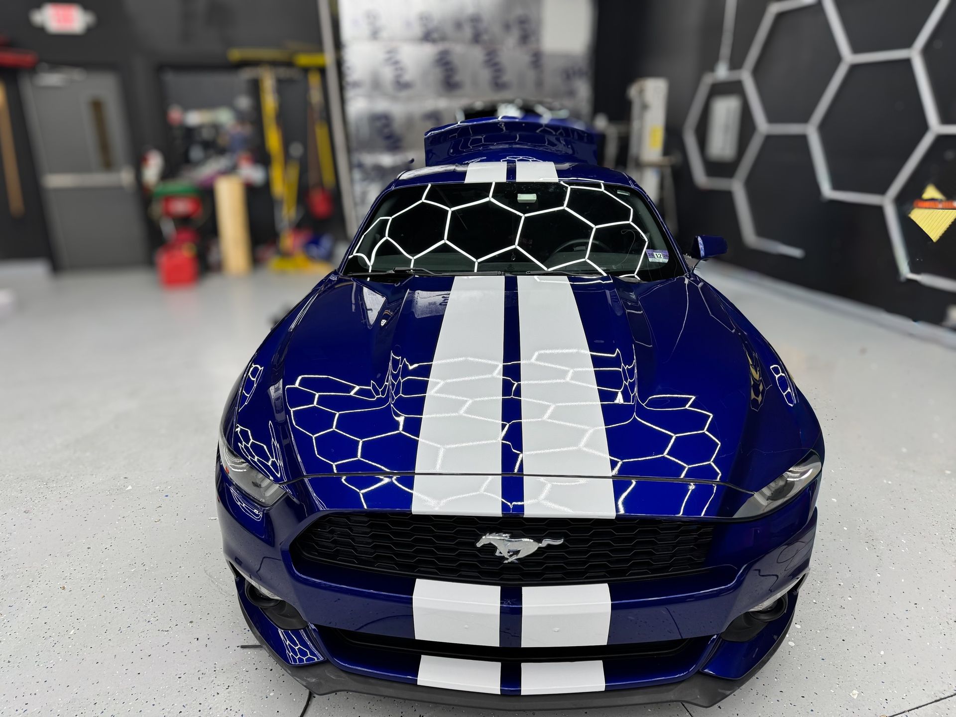 Blue sports car with white racing stripes in a garage, front view