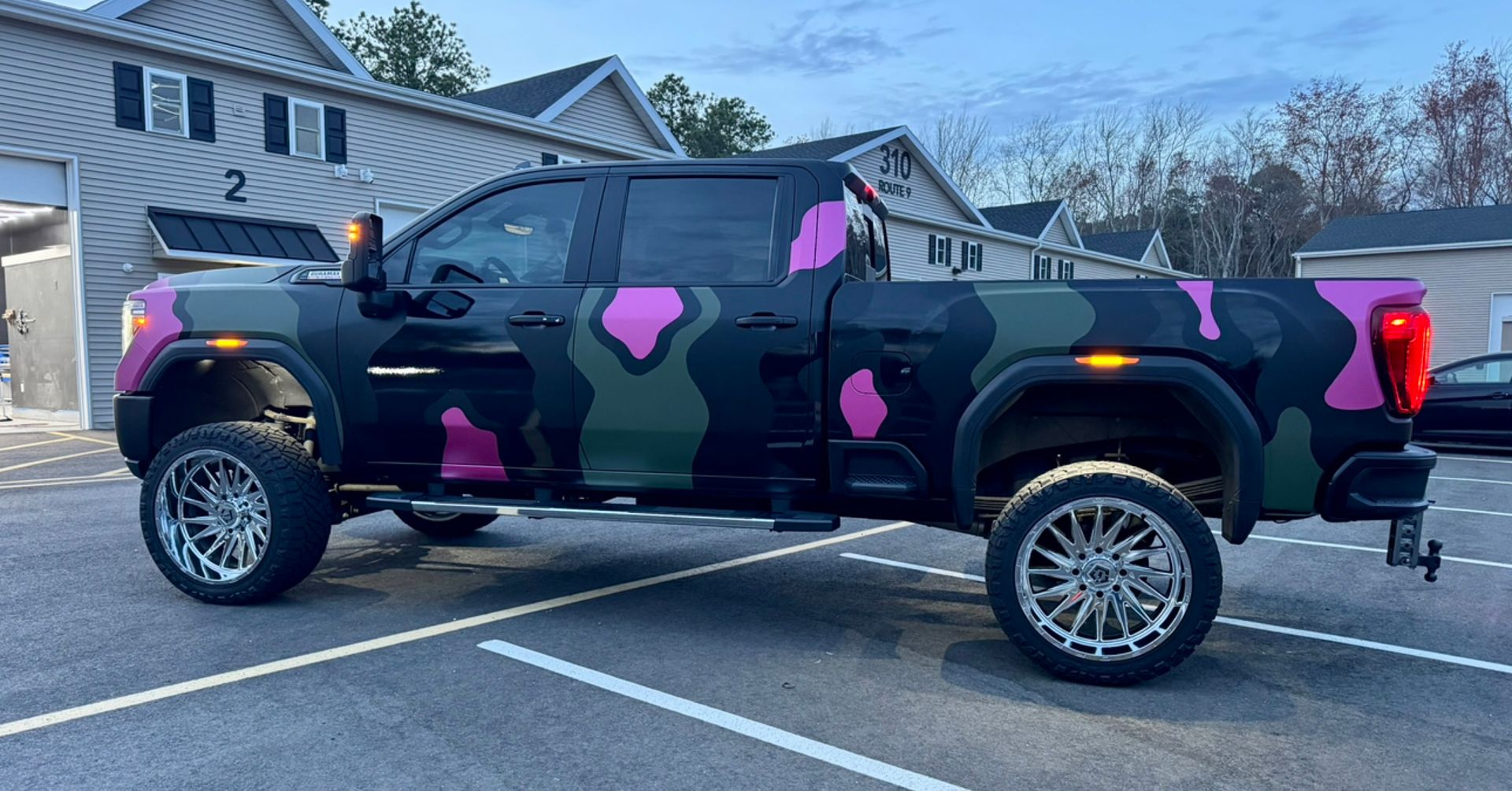 Camouflaged black pickup truck with pink heart decals parked in a lot at dusk