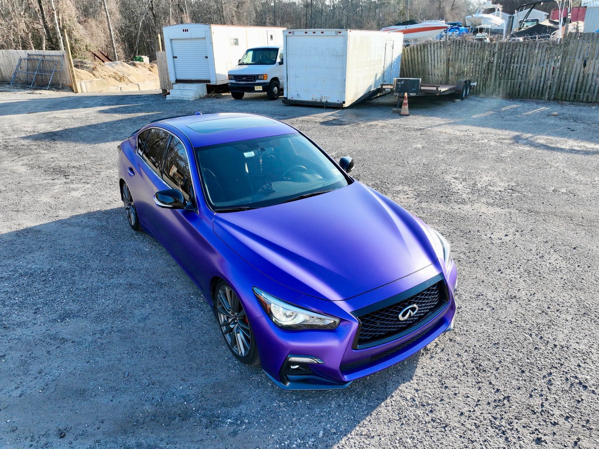 Purple sports sedan parked on gravel lot with trailers in the background
