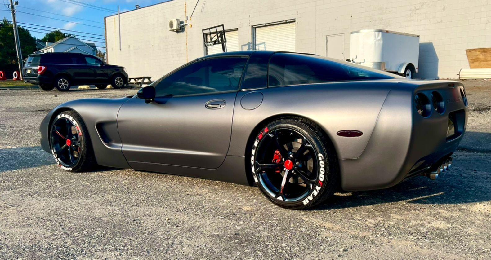 Silver Dodge Challenger parked in a lot beside a beige building, side view with black rims and red brake calipers
