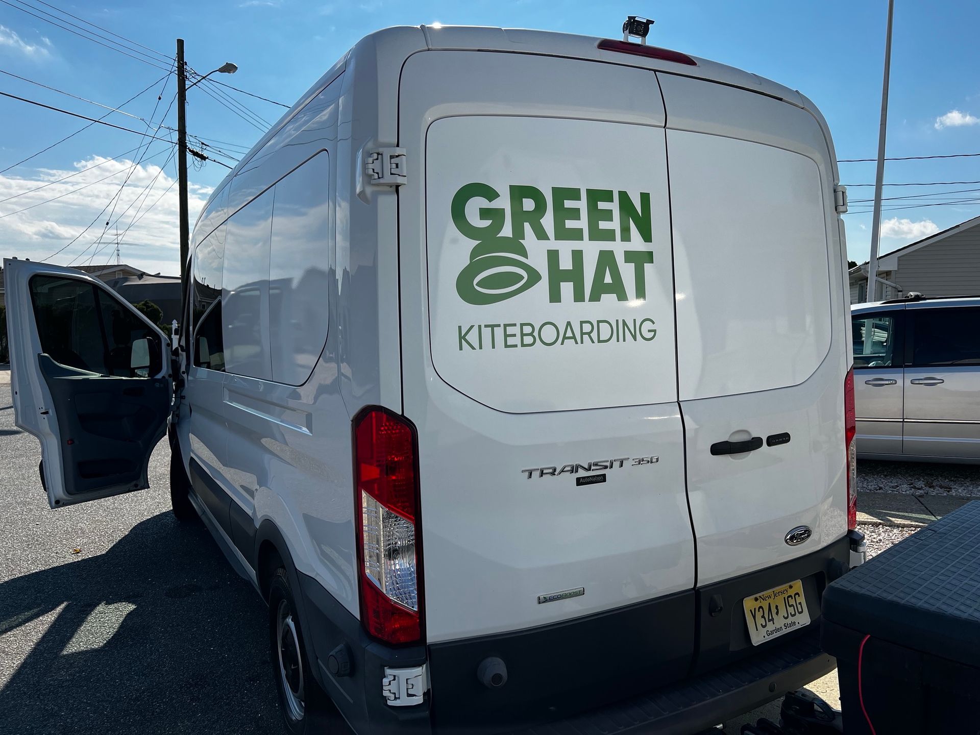 White Green Hat Kiteboarding van parked outdoors under a blue sky.