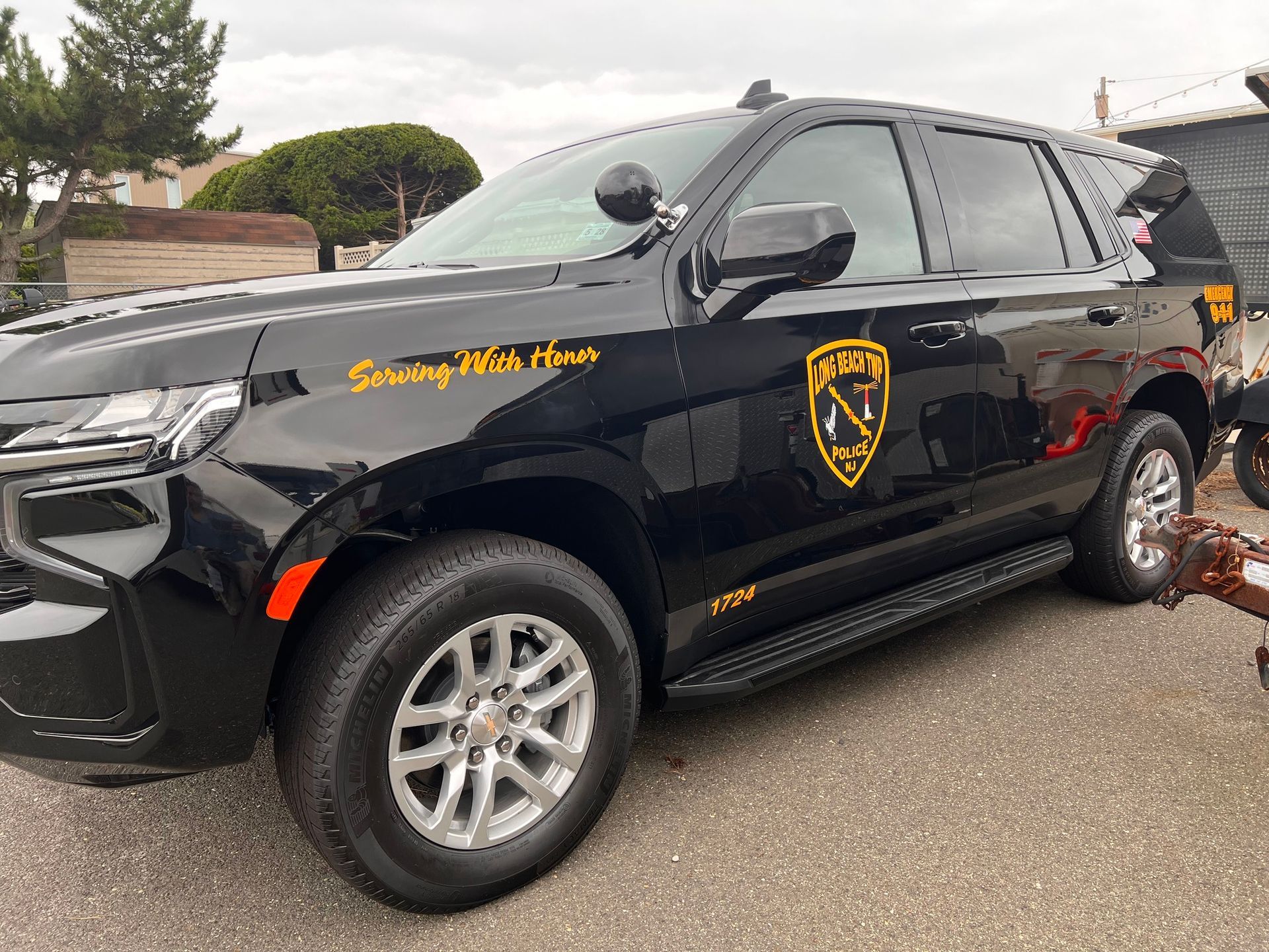 Black security SUV with yellow logo and lettering parked outdoors on a wet street.