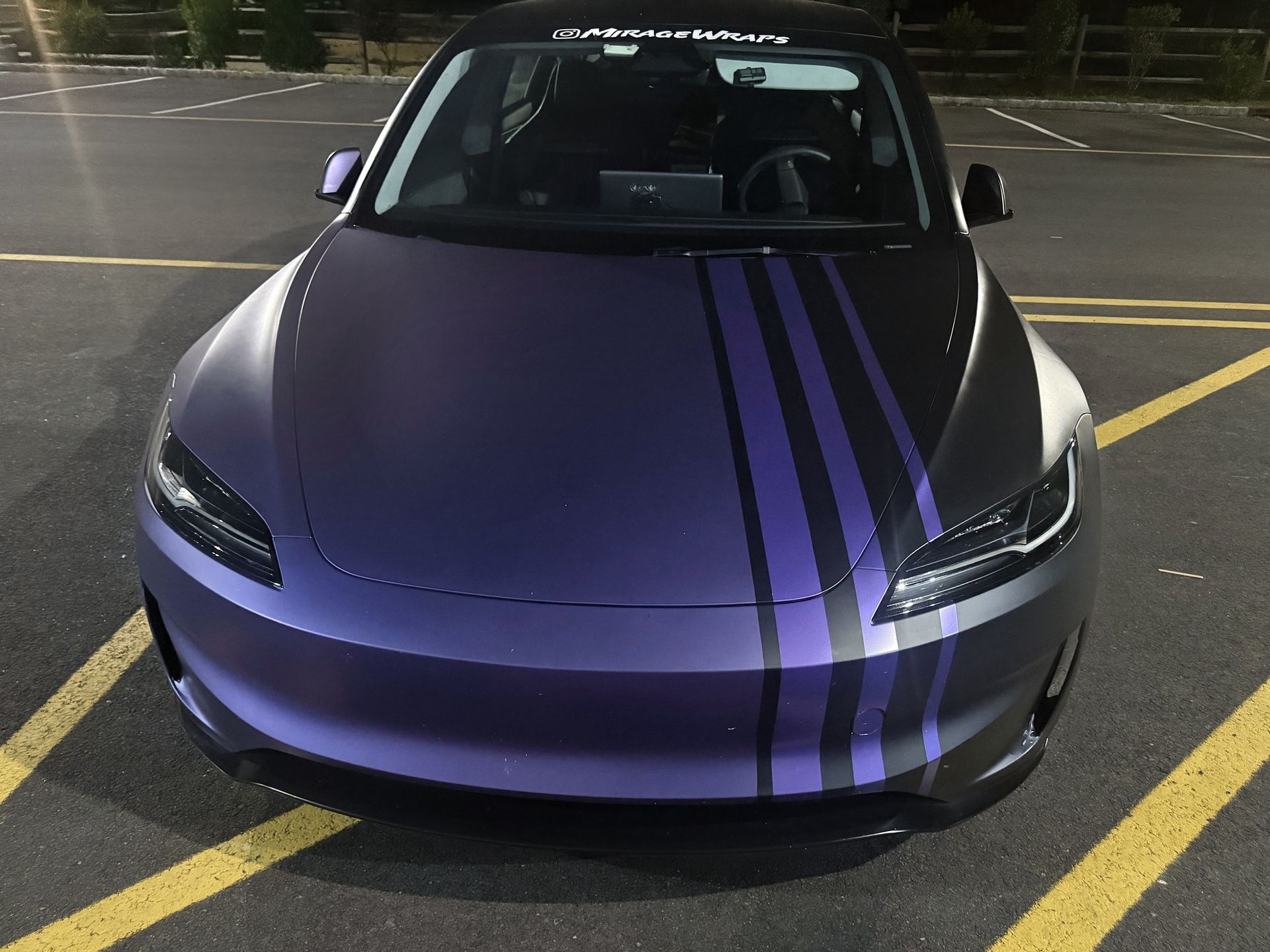 Purple sports car with black racing stripes parked in a striped parking lot.
