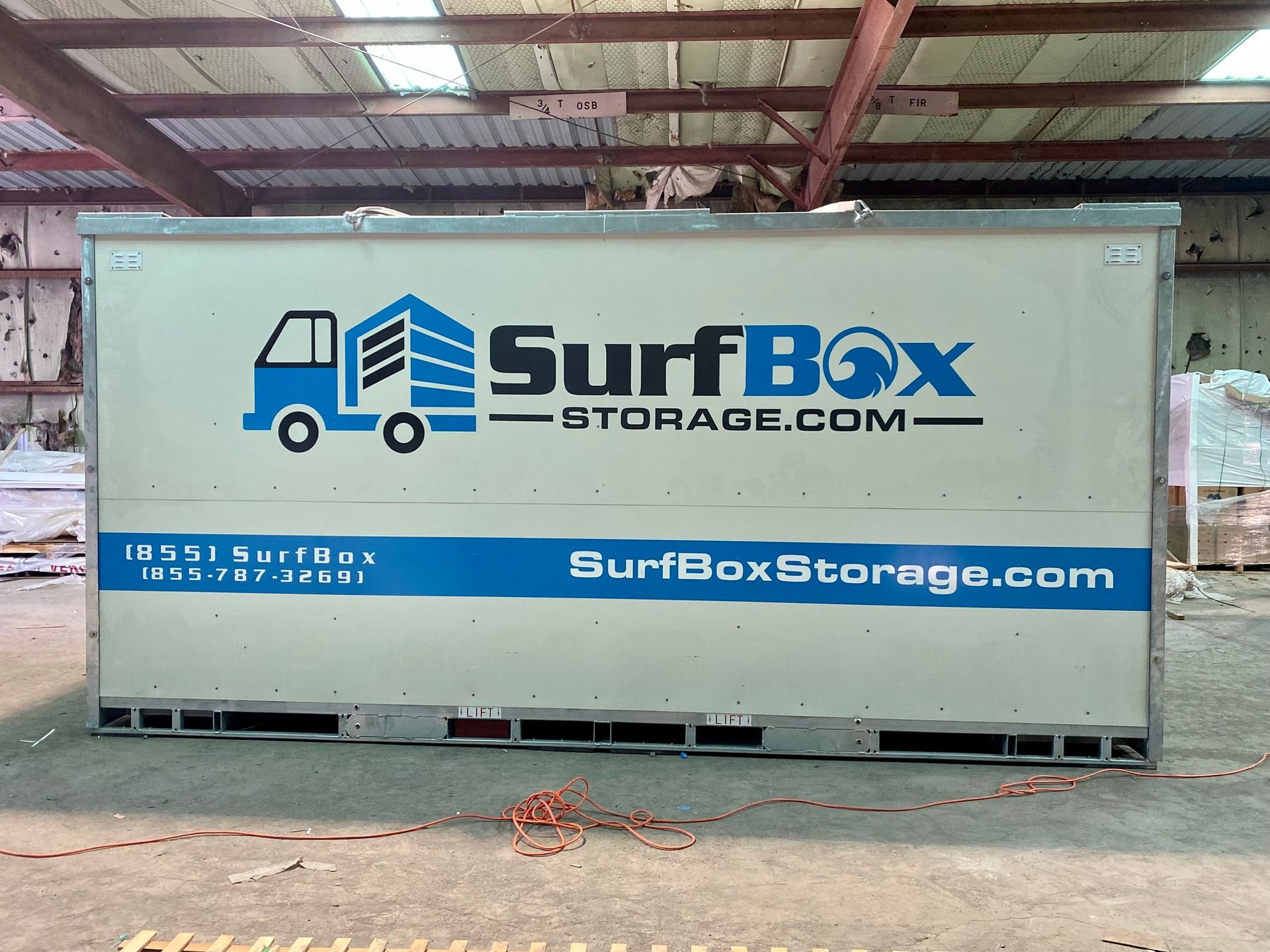 White SurfBoxStorage.com shipping container in a warehouse, with blue truck logo and branding.