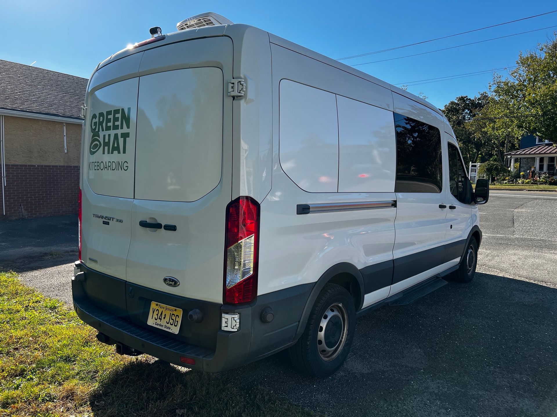 White cargo van with green lettering parked on a sunny gravel lot near trees
