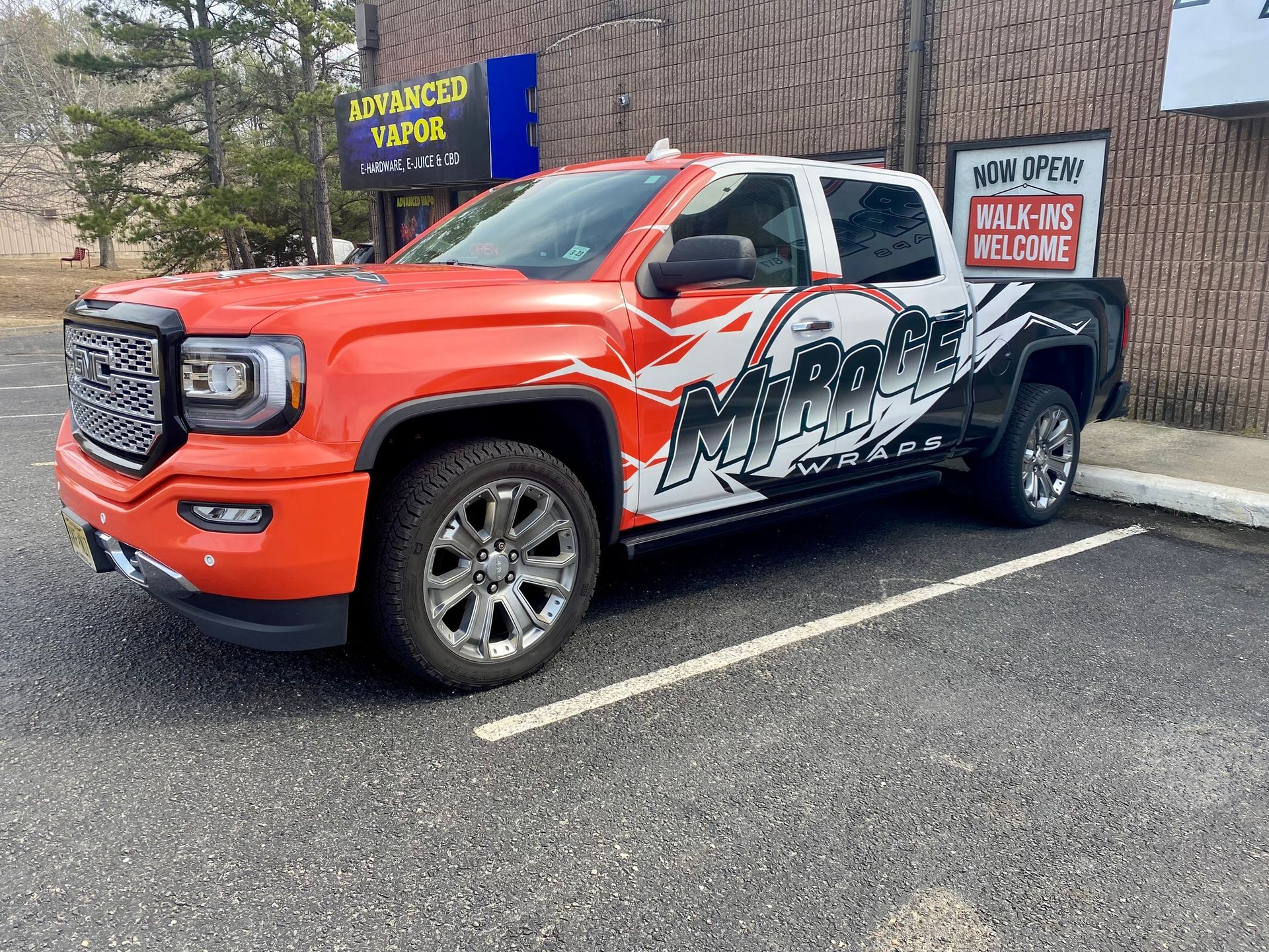 Bright orange and silver pickup truck with wolf graphics parked beside a building.