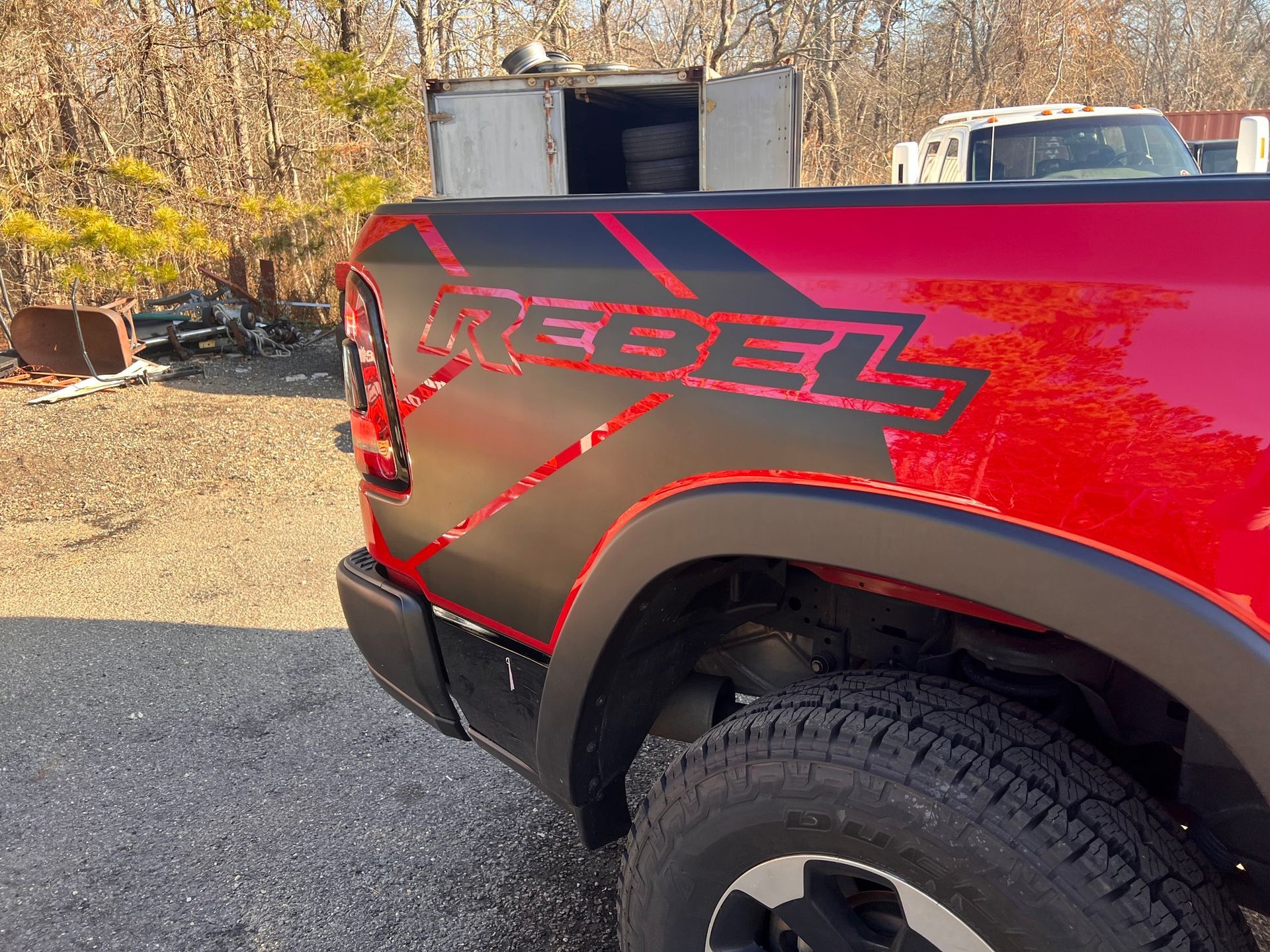 Red pickup truck side with black “Rebel” decal and off-road tire on a gravel lot