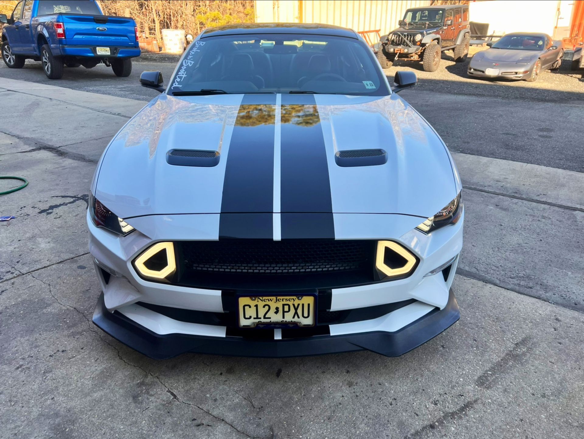 Front view of a white sports car with black hood stripes and neon yellow headlights on a street