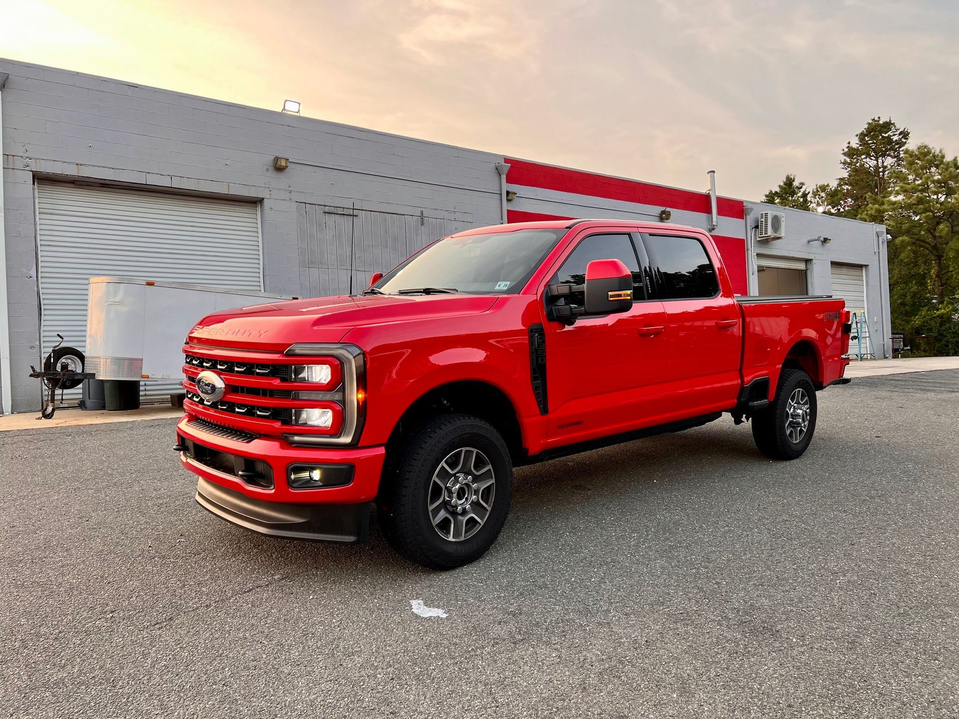 Bright red pickup truck parked outside a white garage at sunset