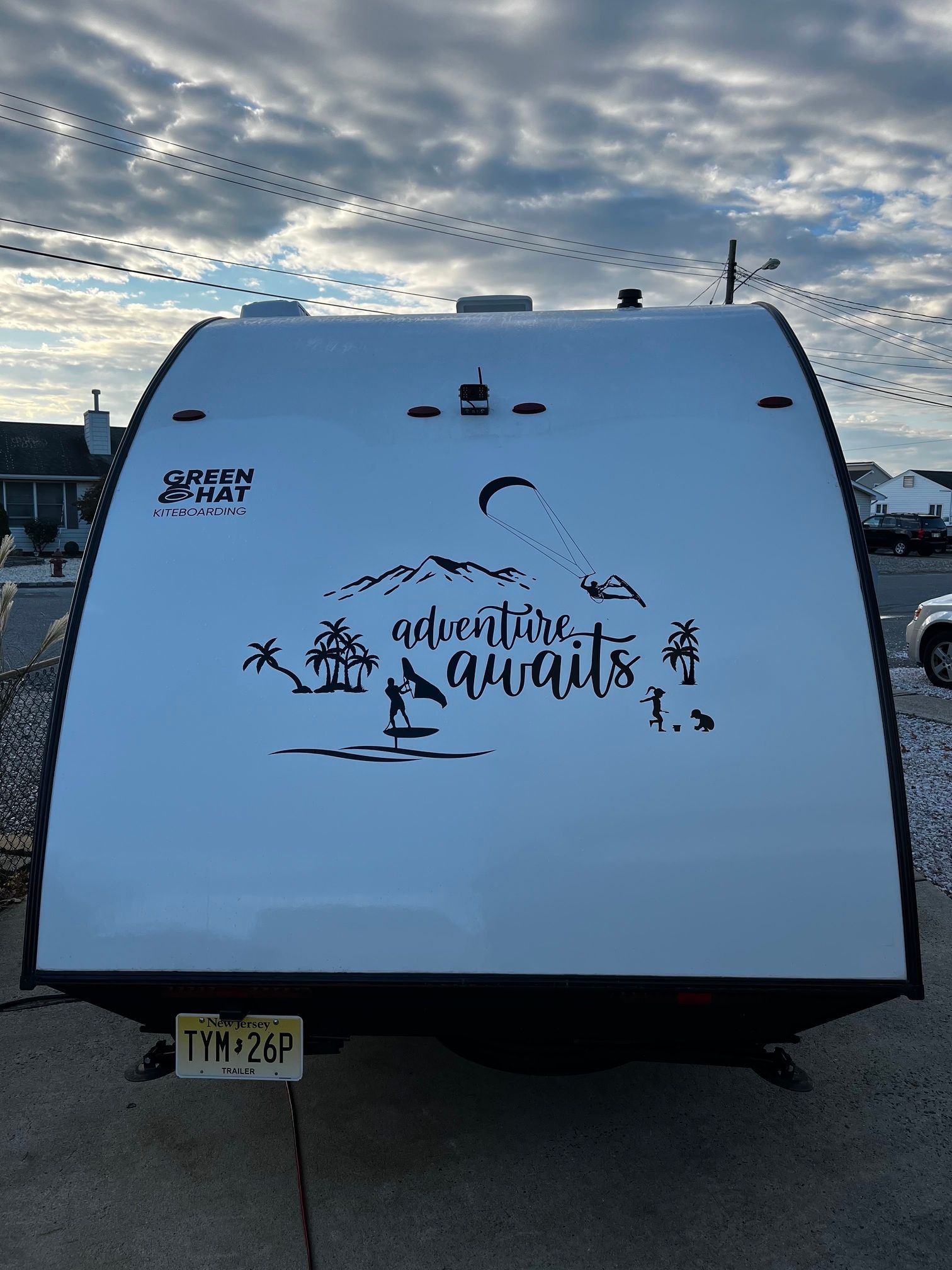 White travel trailer with mountain and palm tree decal, parked outdoors under a cloudy sky.