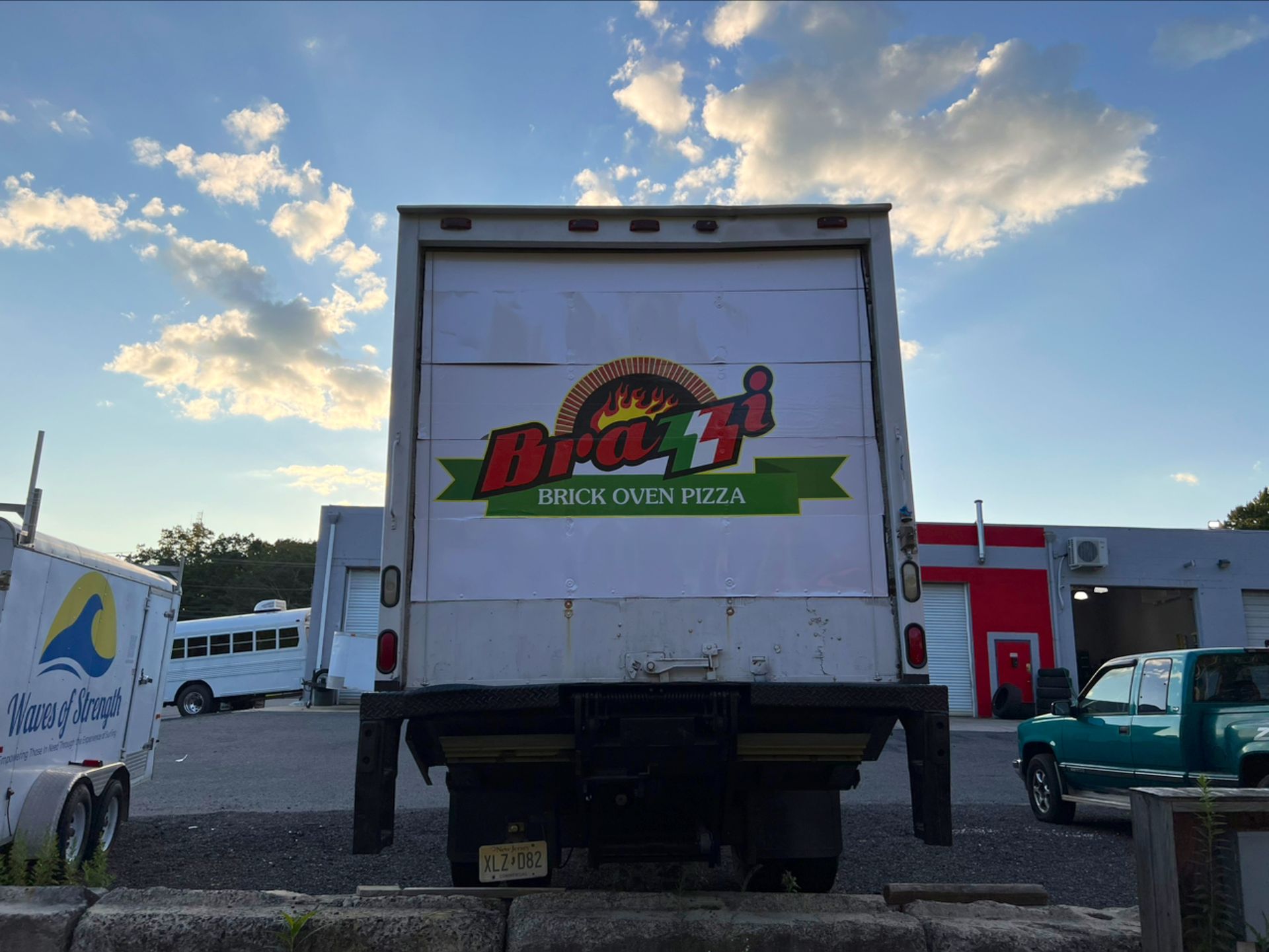Back of a pizza delivery truck with colorful logo, parked in a lot at sunset