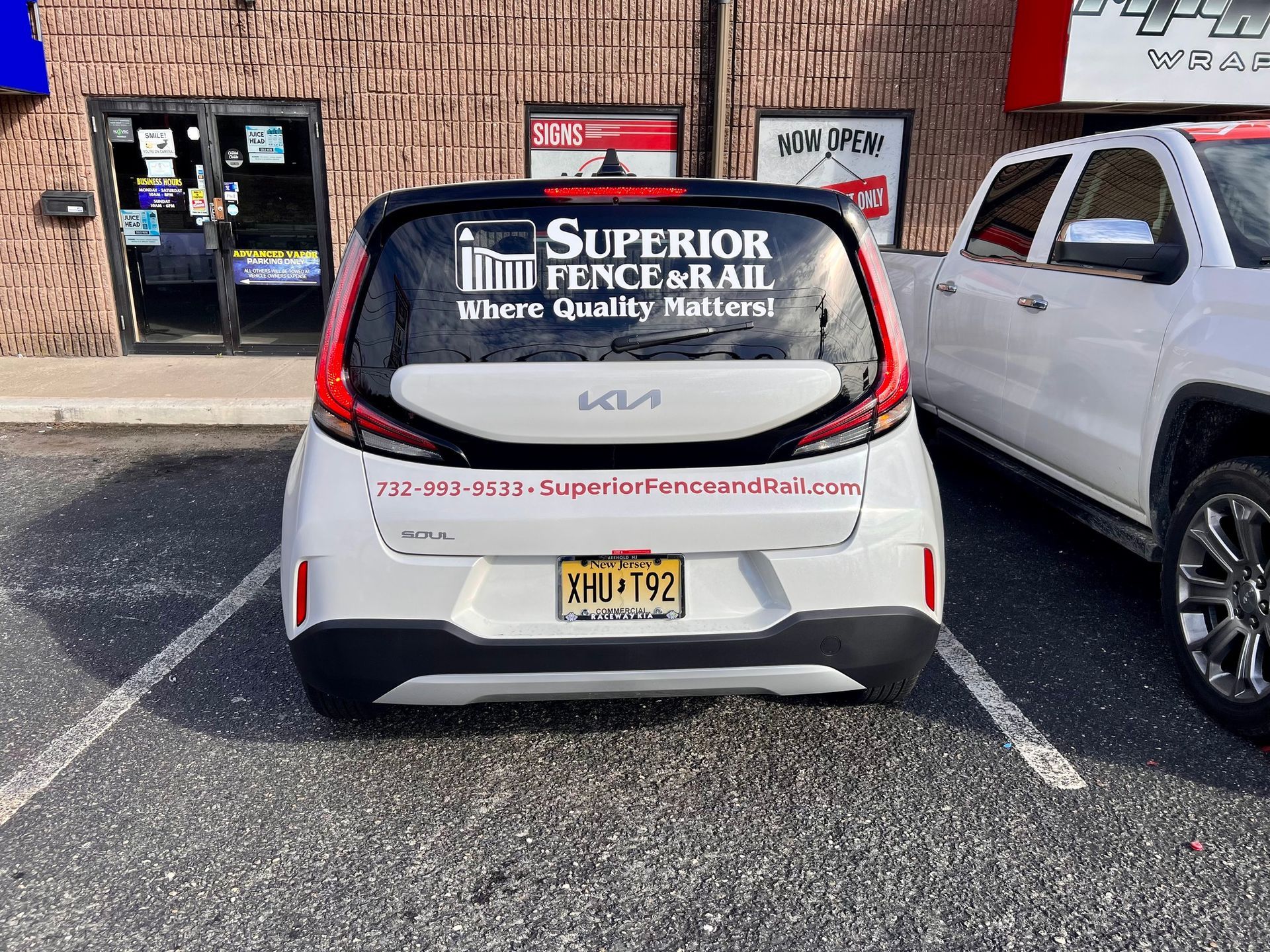 White Kia hatchback with “Superior Window Repair” signage parked outside a brick storefront.