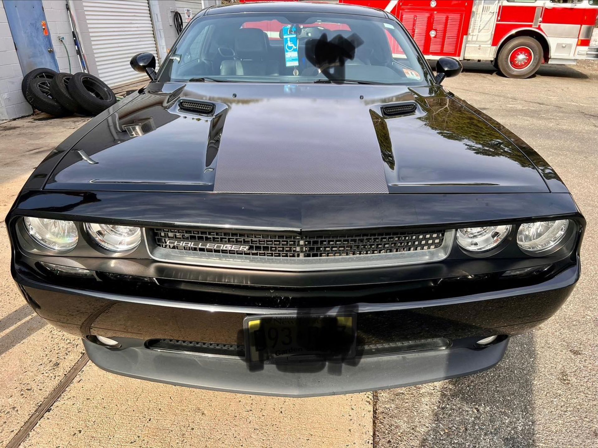 Front view of a black muscle car with dual hood stripes, parked outdoors near a garage.