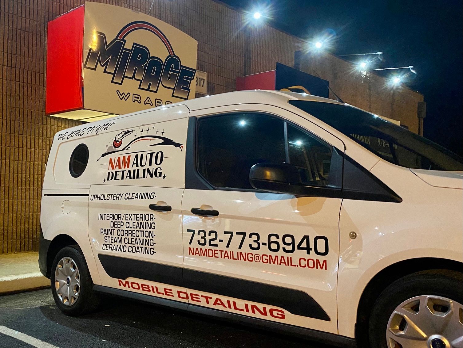 White mobile detailing van with red logos and phone number parked outside at night