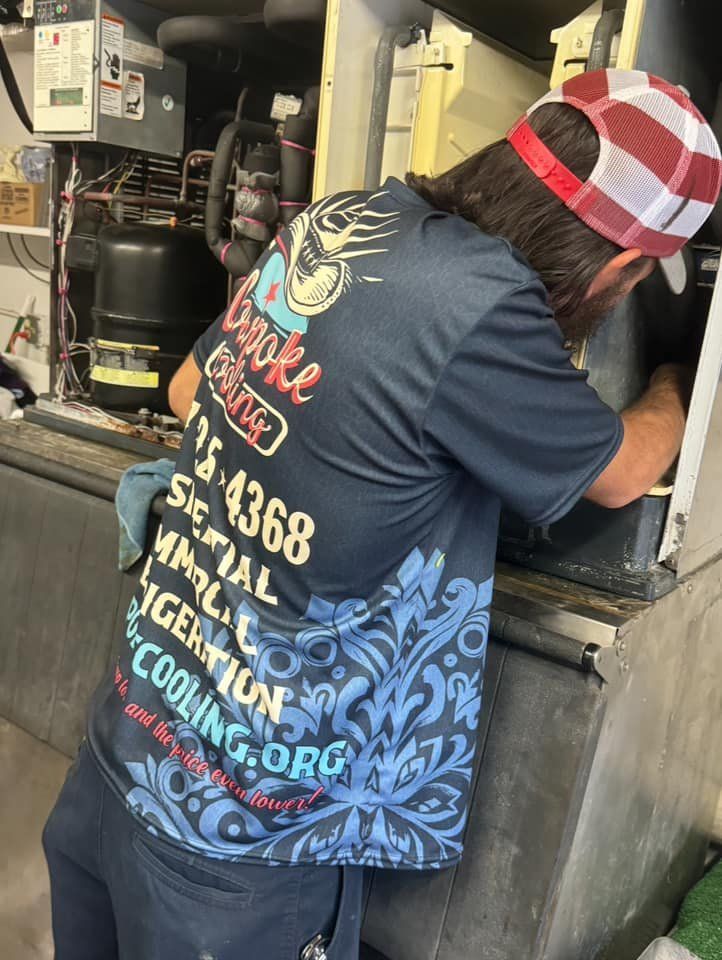 A man wearing a hat and a t-shirt is working on a refrigerator.
