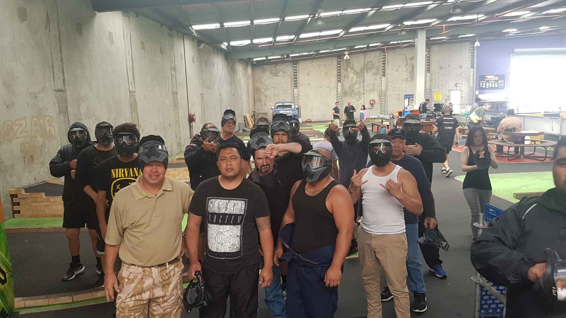 Group of people in a warehouse-like space, walking toward the camera amid industrial equipment and bright overhead lights