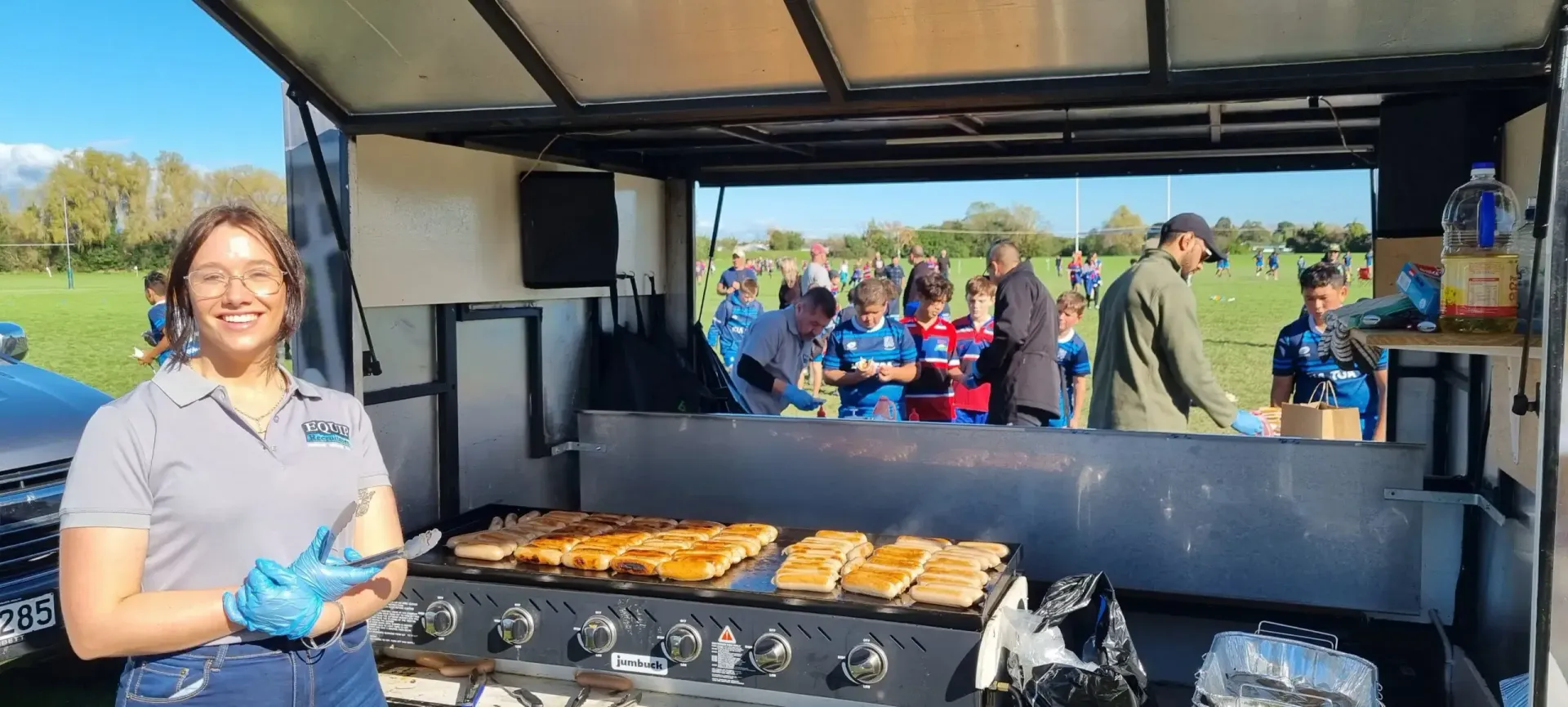 Outdoor food stall with a smiling worker serving grilled food at a charcoal grill