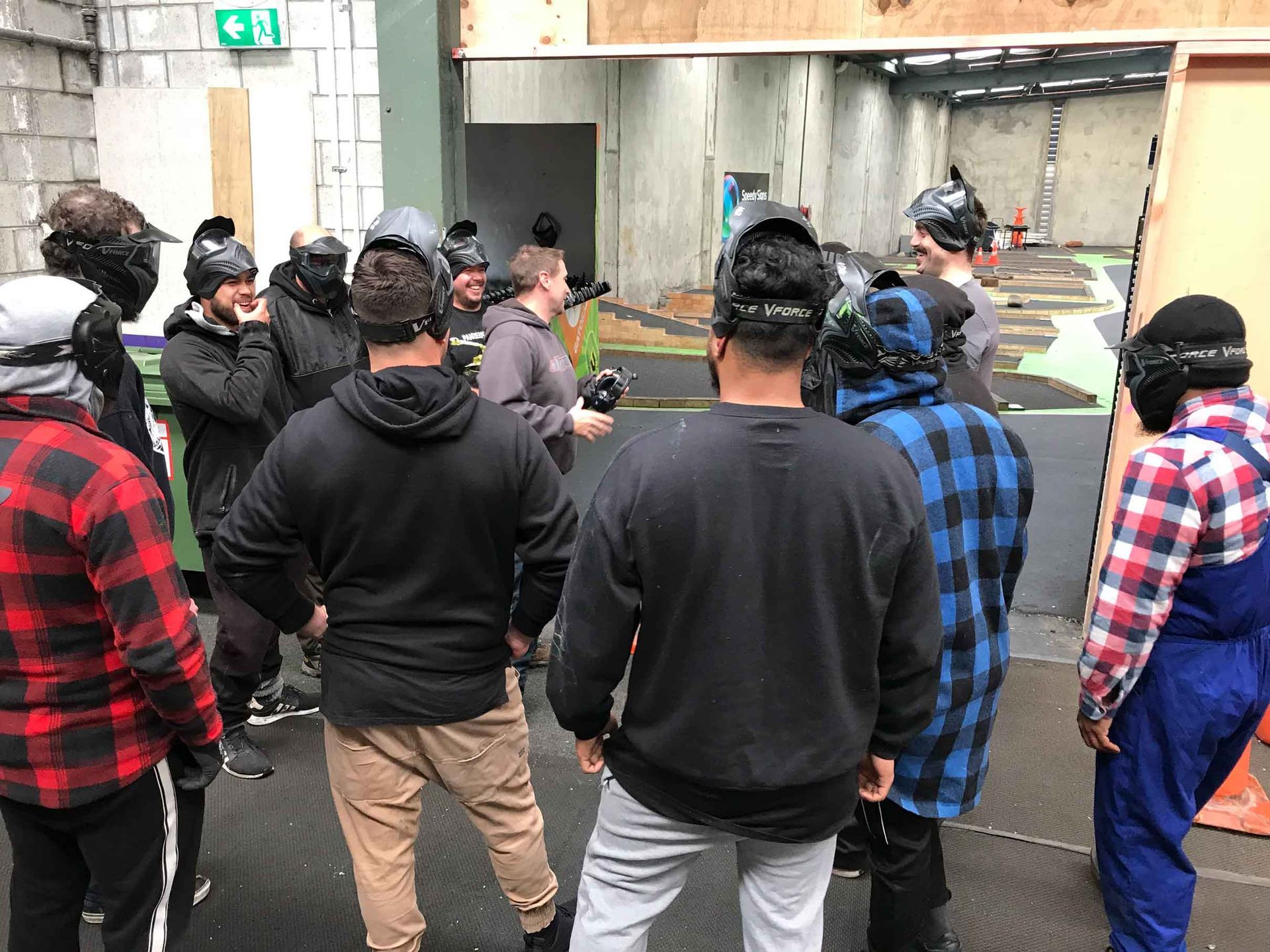 People gathered in a city alley, facing a wall and door, with backpacks and helmets on.