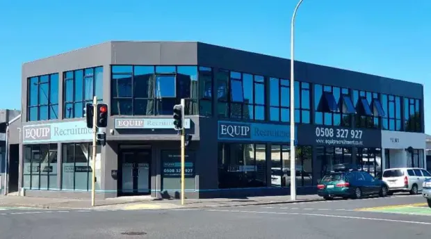 Blue two-story commercial building on a street corner with large windows and storefront signs.