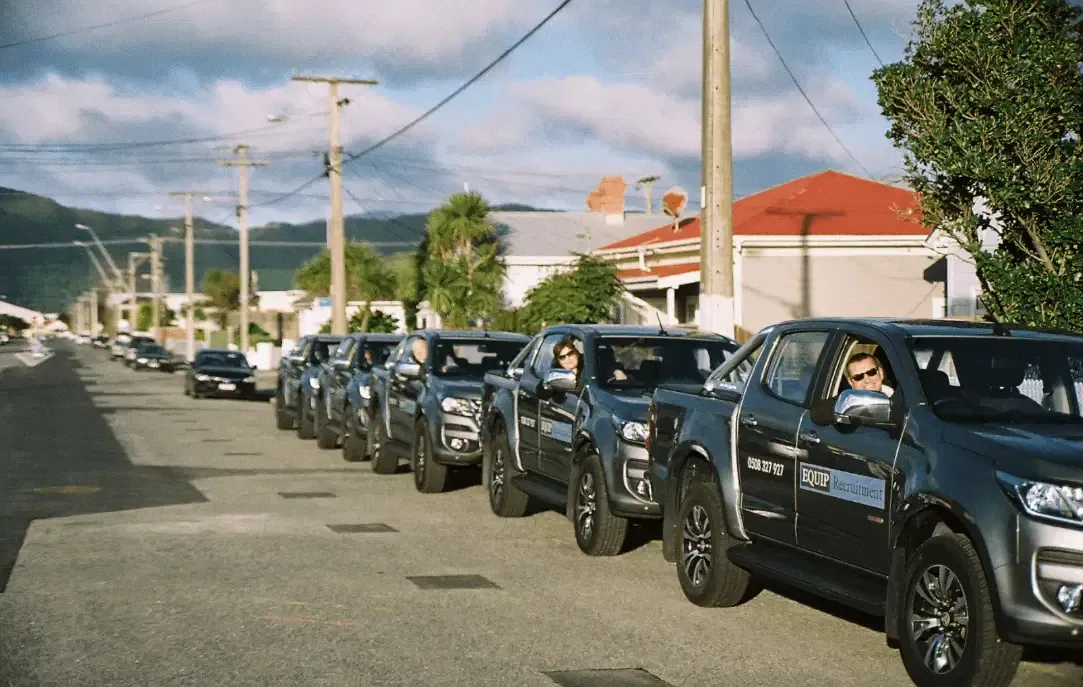 Line of black pickup trucks parked along a sunny street with homes and mountains in the background