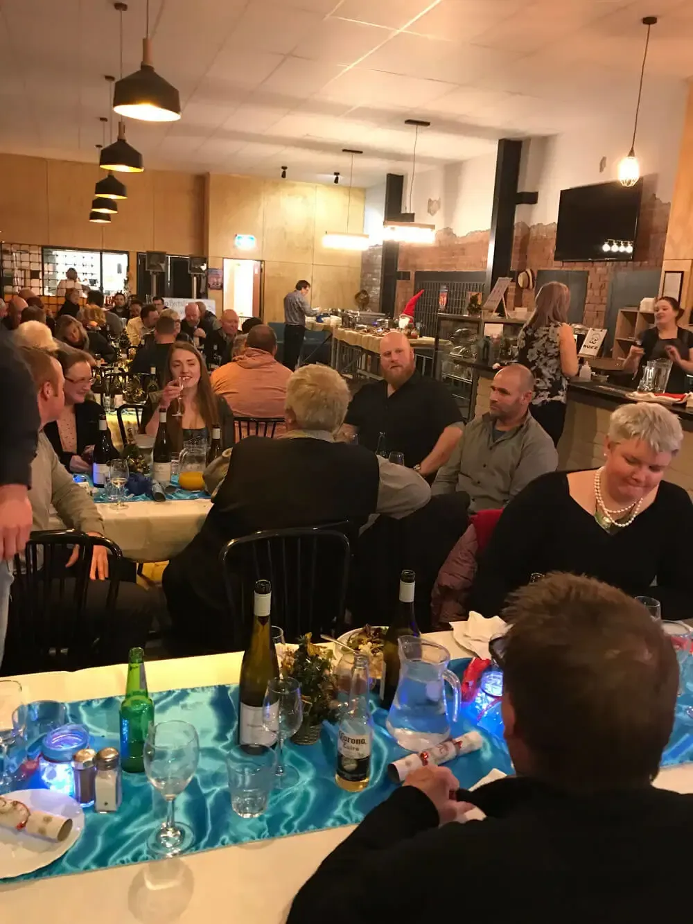 Crowded restaurant with people dining at tables under warm hanging lights