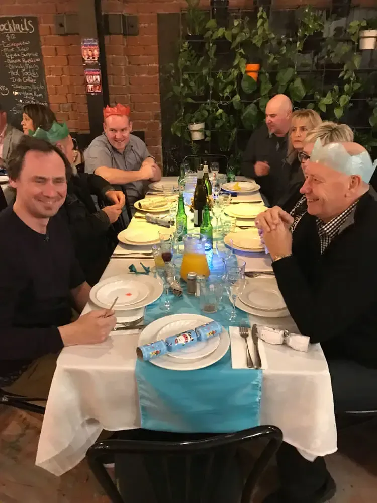 Five people seated at a restaurant table with plates, glasses, and bottles, smiling and chatting