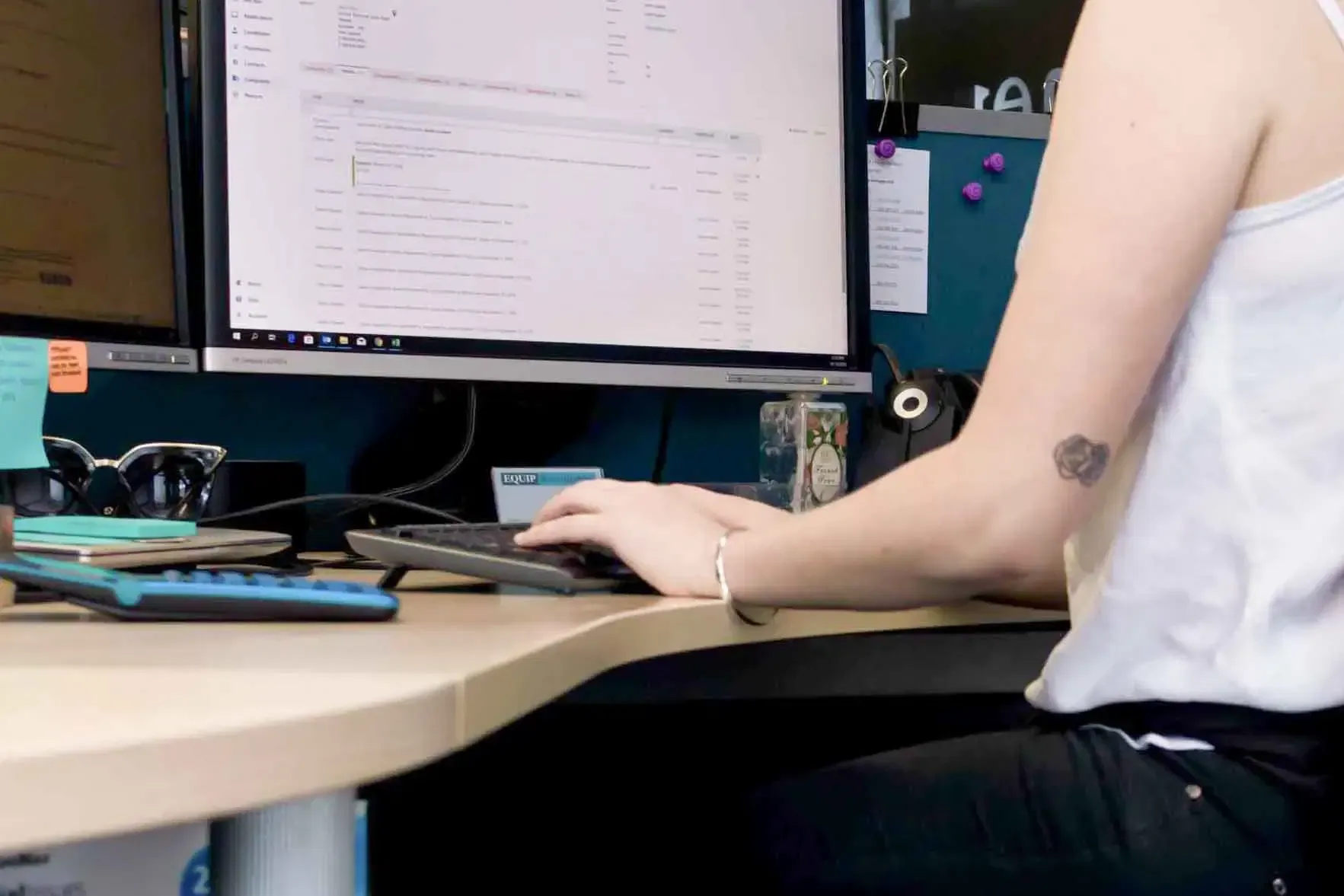 Person at a desk typing on a keyboard beside a monitor in an office workspace